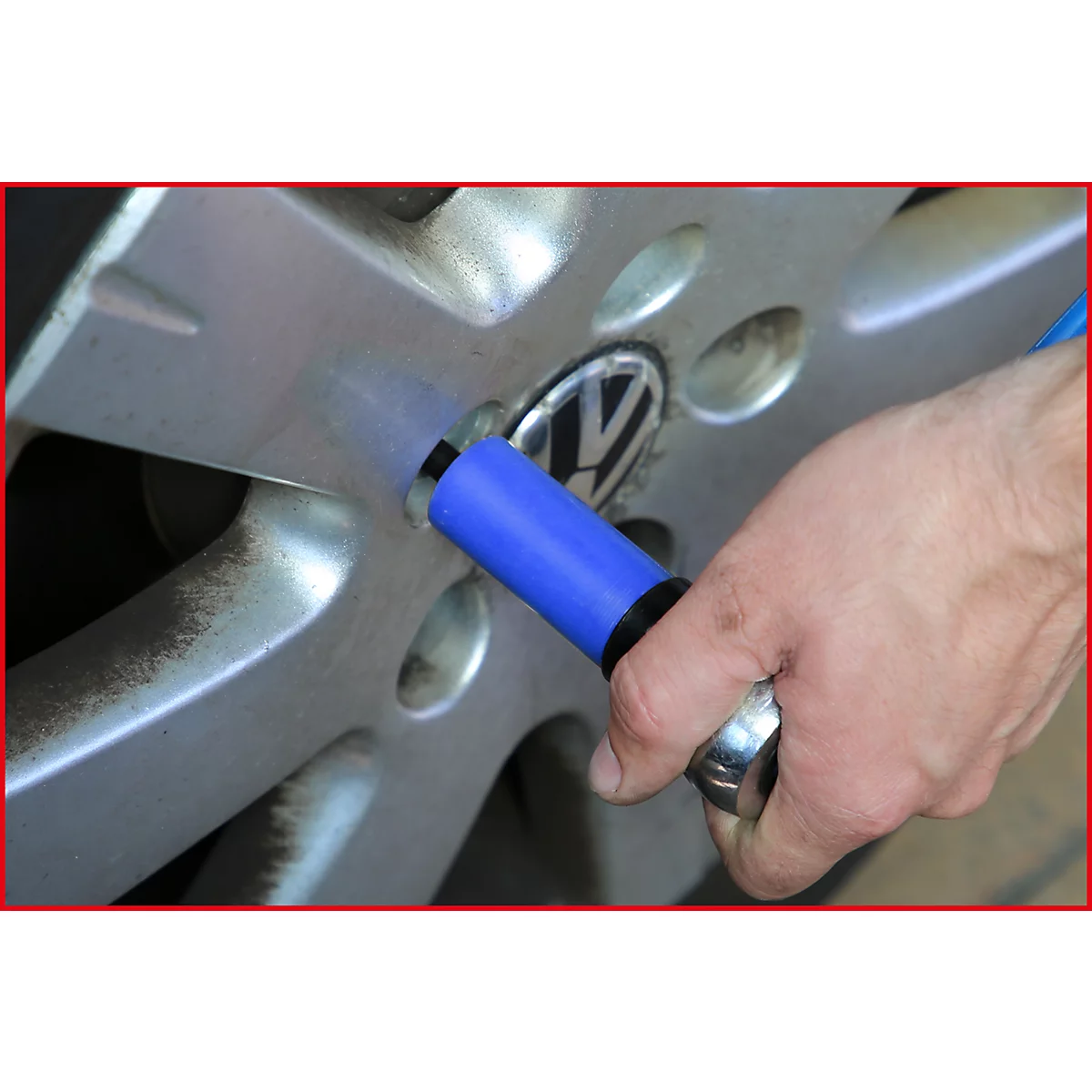 Nahaufnahme eines silbernen Autorads, an dem eine blaue Steckschlüssel-Nuss angebracht wird. Im Hintergrund ist das VW-Logo zu sehen.